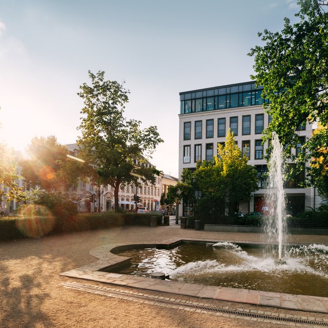 freier platz mit springbrunnen, bäumen und gebäude im hintergrund